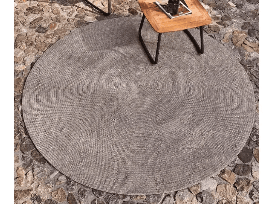 Der runde Weishäupl Outdoor-Teppich in Sand auf einer Holzterrasse mit modernen Gartenmöbeln